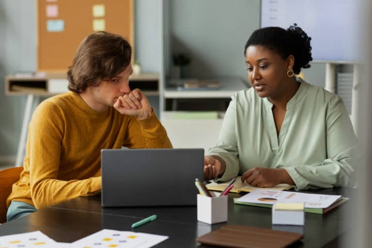 Two professionals collaborating on mentorship software at a desk.