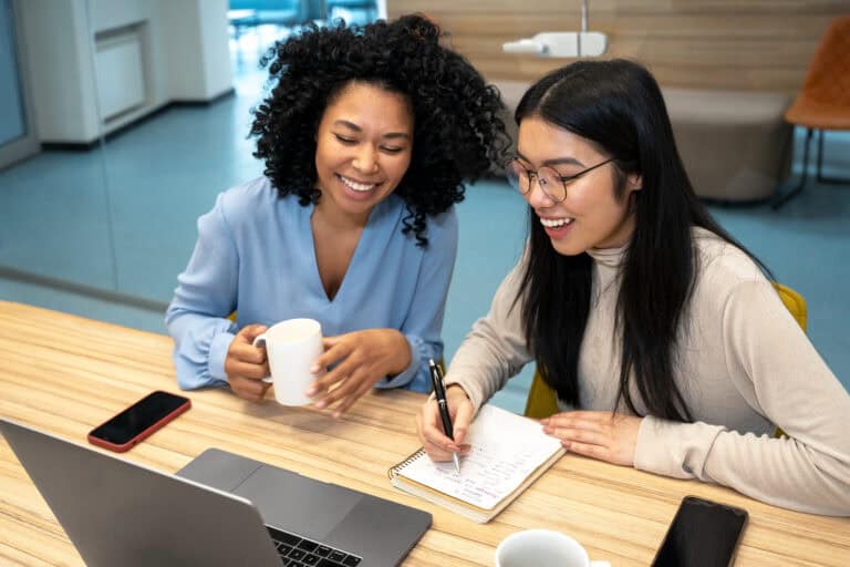 Two women collaborating with mentorship software on a laptop for employee retention.