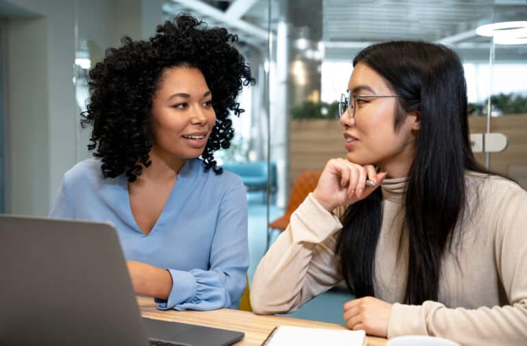 Two women engaged in a virtual mentorship discussion in a modern office setting.
