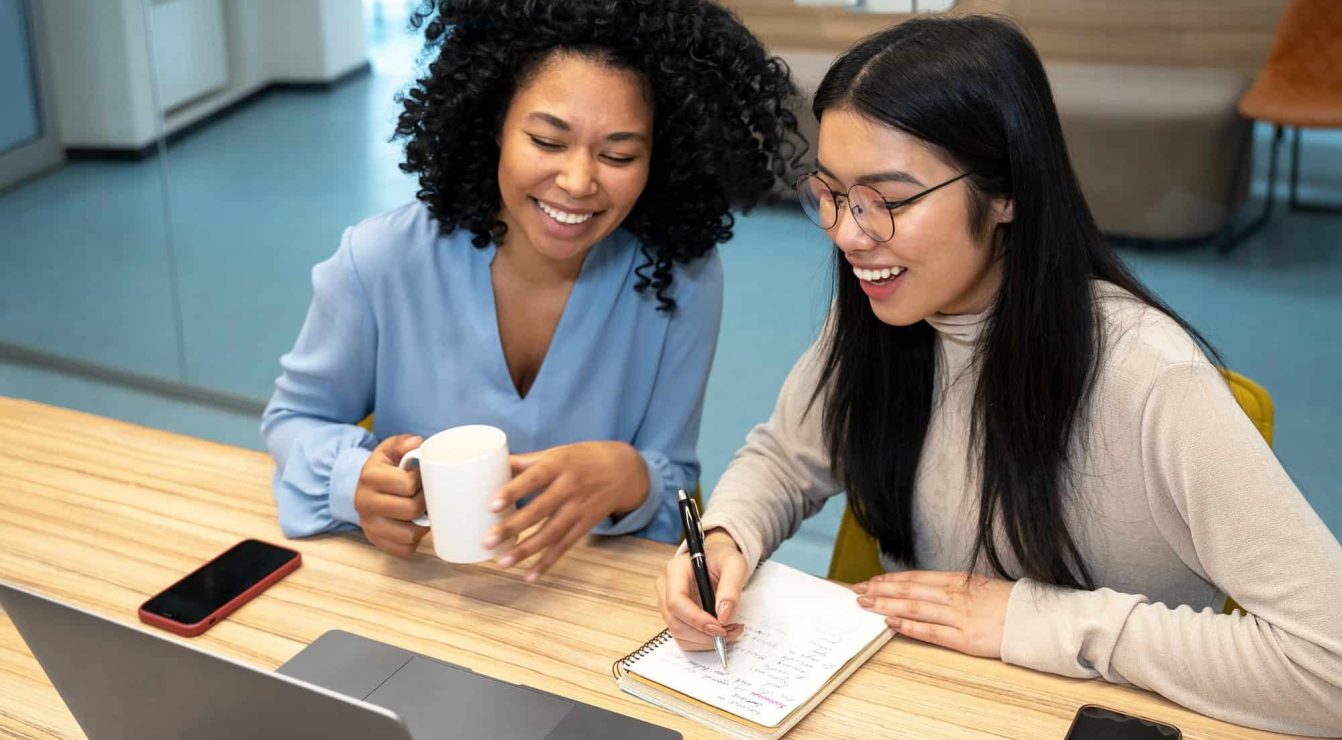 Two women collaborating with mentorship software on a laptop for employee retention.